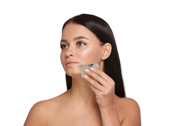 Beautiful girl with natural makeup and clean skin Holds in hand a jade face scrubber