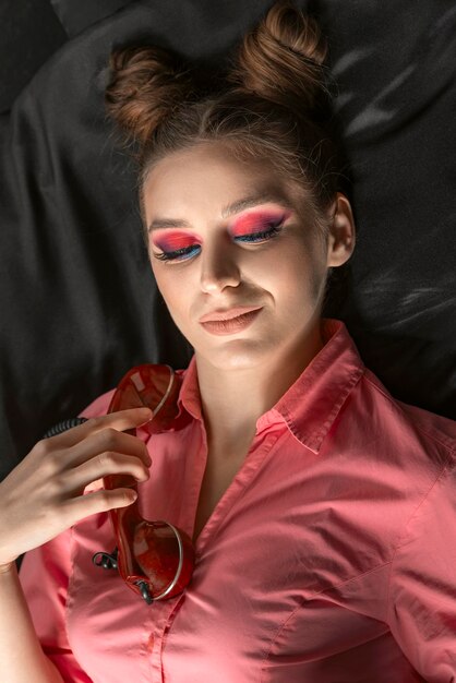 Beautiful girl with pink eyeshadow and bun hairstyle with retro landline phone on black background Vertical frame