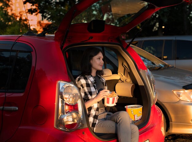 Beautiful girl with popcorn and fried chicken sitting in the car while watching a movie at drive in cinema Selective focus Entertainment leisure activities hobby concept