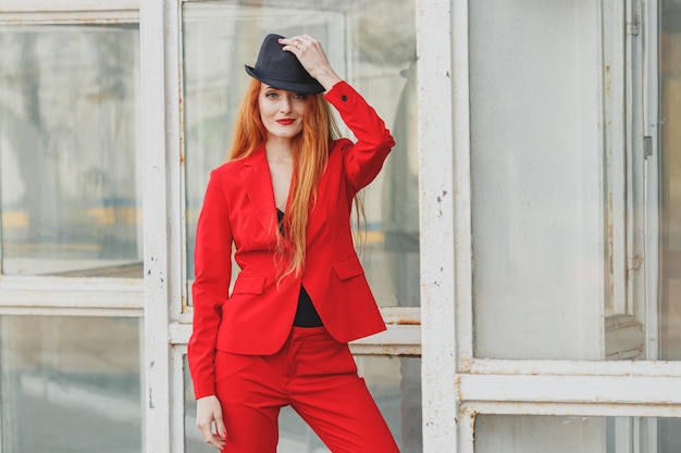 Photo beautiful girl with red hair dressed in a red business suit business portrait