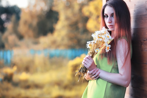 Beautiful girl with red hair with a bouquet of daisies on the nature