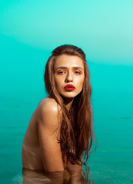 Beautiful girl with red lipstick and naked torso stands in the sea.