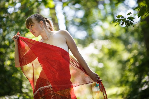 Beautiful girl with red scarf stands in thicket of forest