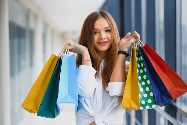 Beautiful girl with shopping bags is looking at camera and smiling while doing shopping in the mall