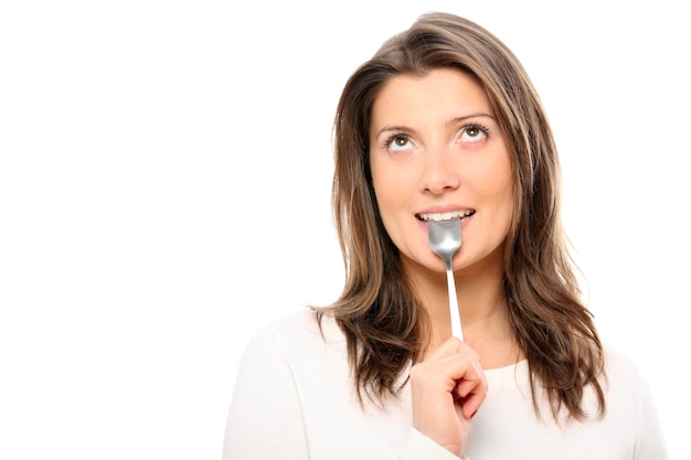 a beautiful girl with a teaspoon in her mouth standing against white background