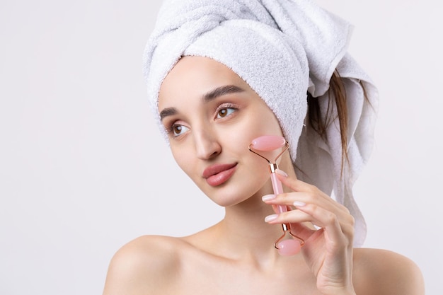 Beautiful girl with thick eyebrows and perfect skin at white background towel on head beauty photo Holds a cosmetic roller