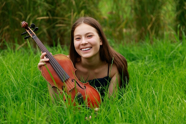 Beautiful girl with violin smiling in nature. High quality photo