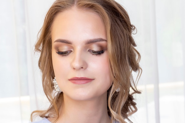 Beautiful girl with a wedding hairstyle looks at herself in the mirror, portrait of a young girl. beautiful make-up. beauty saloon