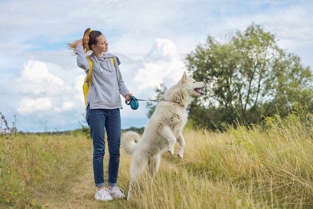 Beautiful girl with white dog, teenager walking with husky pet