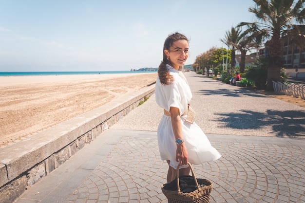 Beautiful girl with a white dress and a bag walking thorugh a coast village