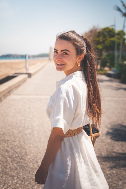 Beautiful girl with a white dress and a bag walking thorugh a coast village