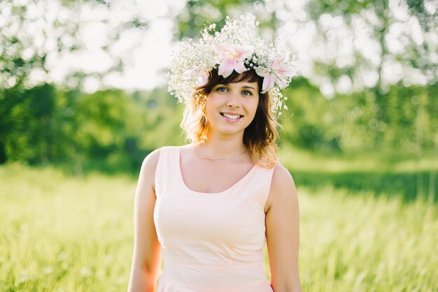 Beautiful girl with a wreath of flowers on her head smiling outdoors on a Sunny day