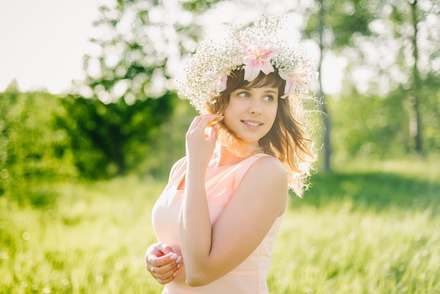 Beautiful girl with a wreath of flowers on her head smiling outdoors on a Sunny day