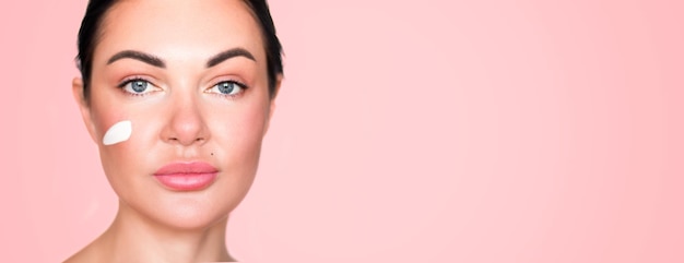 Beautiful girl woman Portrait Collected hair Beauty photo Clean skin Pink background A smear of cream on the cheek