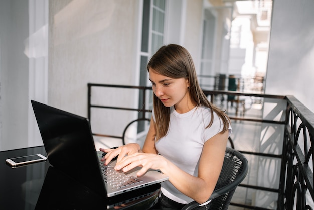 A beautiful girl works with her laptop on the balcony on a summer day.