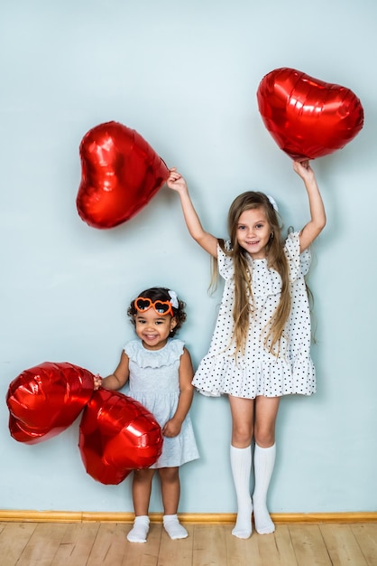 Beautiful girls, white and with dark skin color, celebrate valentine's day. heart shaped red foil balloons