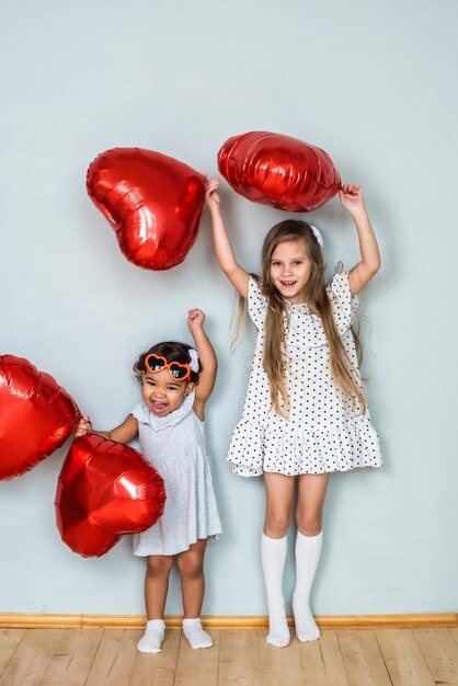 Beautiful girls white and with dark skin color celebrate valentines day heart shaped red foil balloons