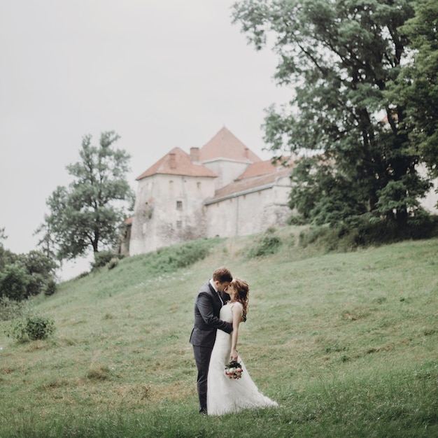 Beautiful gorgeous bride and groom walking in sunny park and kissing happy wedding couple hugging in green garden at old castle happy romantic moments elopement concept