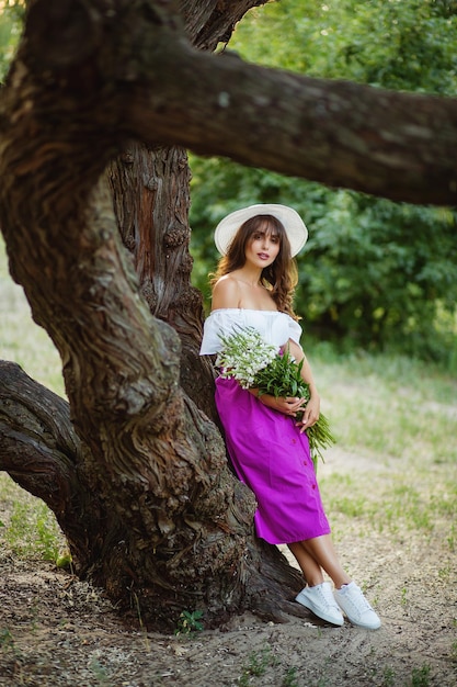 Beautiful graceful lady in hat near the old mighty tree