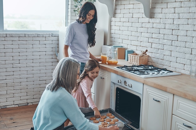 Beautiful grandmother taking out cookies from the oven and smiling while spending time with family