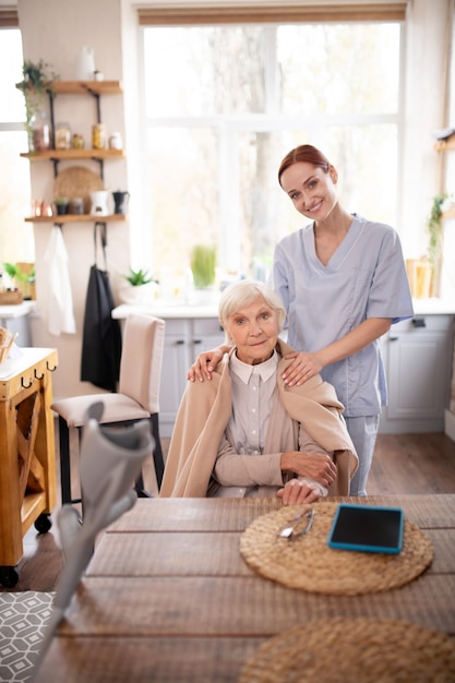 Beautiful grey-haired pensioner sitting near her caregiver