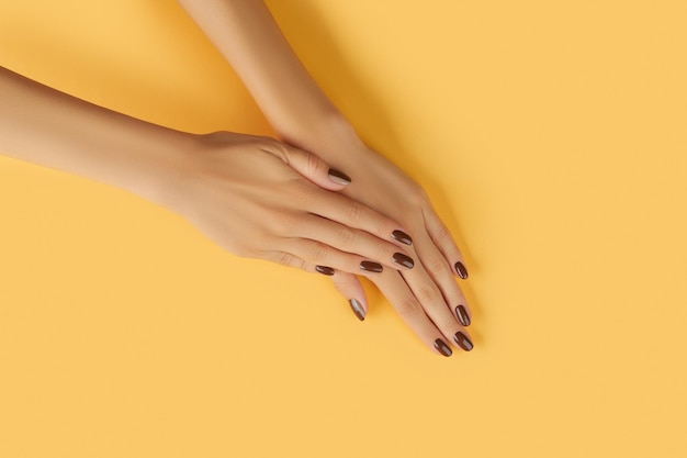 Beautiful groomed womans hands with brown nail design on yellow background