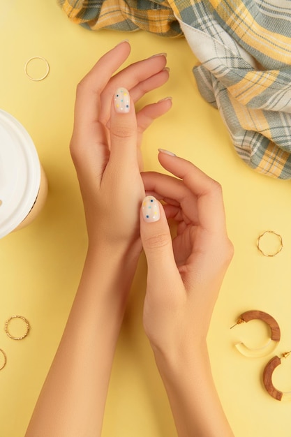 Beautiful groomed womans hands with summer nail design on yellow background