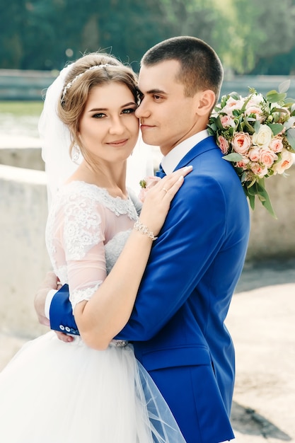 Beautiful guy and girl, bride in a white wedding dress, groom in a classic blue suit against a nature background. Wedding, family creation.