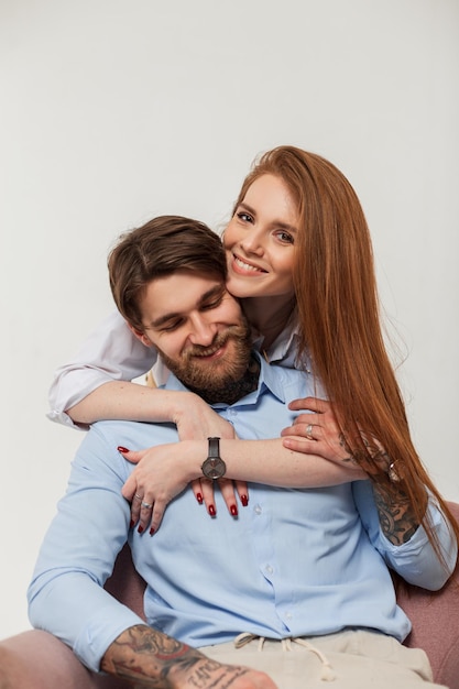 Beautiful happiness fashion couple pretty smiling redhead woman and stylish hipster handsome man sits and hug on a white background