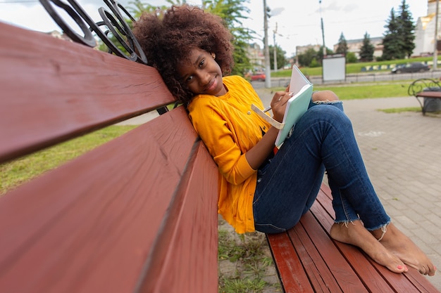 The Beautiful and happy African American woman in the park, makes notes in a notebook