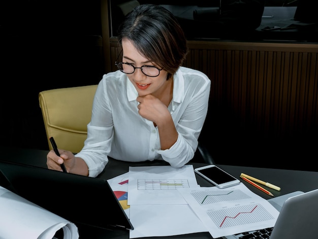 Beautiful happy Asian woman working overtime with laptop computer on desk in office