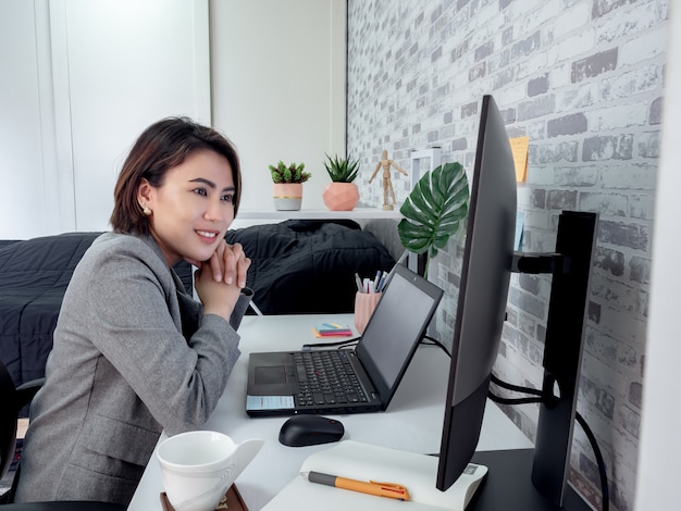 Beautiful happy Asian woman working with laptop computer in her room, condominium.