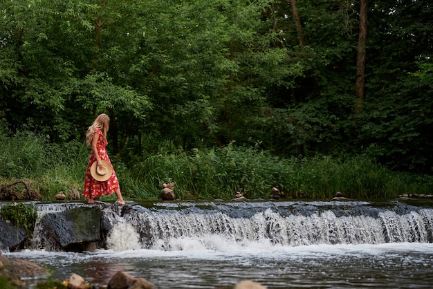 Beautiful happy blonde in a summer dress and a straw hat stands in the water