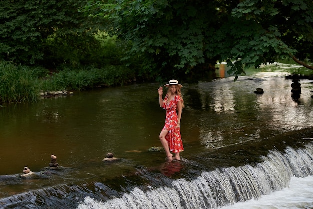 Beautiful happy blonde in a summer dress and a straw hat stands in the water