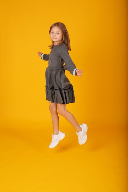 beautiful happy brownhaired girl in a gray school dress jumps yellow background