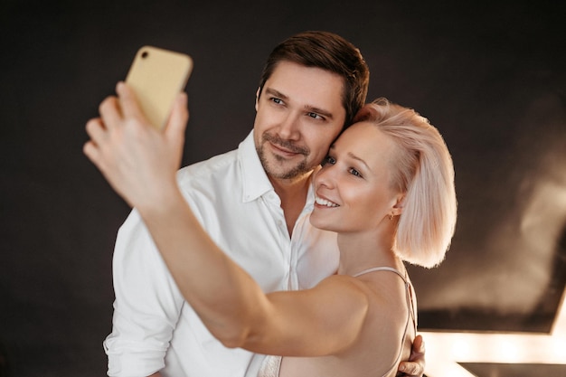 Beautiful happy couple young family in evening dresses taking selfie on mobile phone