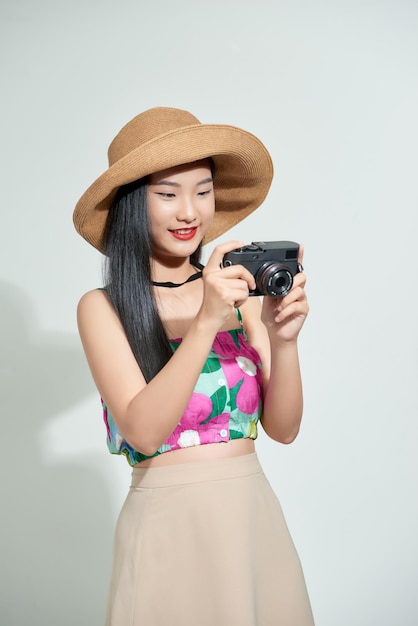 Beautiful happy cute asian woman in casual summer clothes takes photos holding retro photographic camera isolated on a white in hat