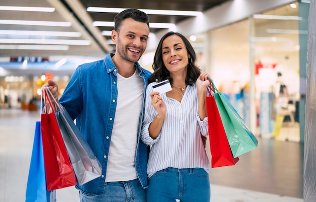 Beautiful happy excited couple in love or family with paper bags and credit card in hands while walking during shopping in the mall