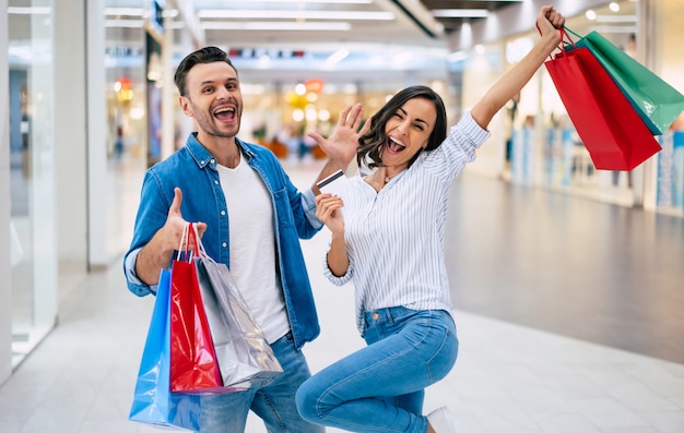 Beautiful happy excited couple in love or family with paper bags and credit card in hands while walking during shopping in the mall