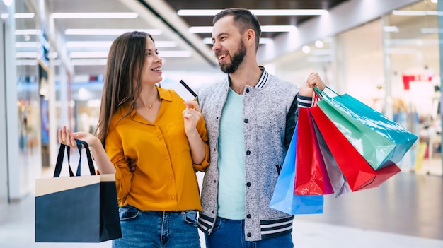 Beautiful happy excited couple in love or family with paper bags in hands while walking during shopping in the mall