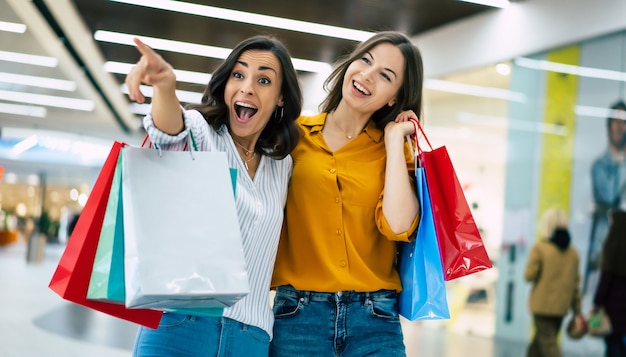 Beautiful happy and excited young girl friends with paper bags are walking around the shopping mall