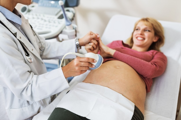 Beautiful and happy expectant mother at gynecological examination with ultrasound medical equipment.