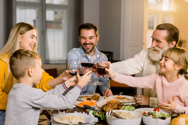 Beautiful happy family clinking glasses of wine and juice on holiday dinner