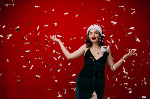 Beautiful happy girl in a santa hat throws confetti New year concept