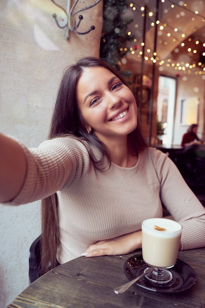 Photo beautiful happy girl taking a selfie in cafe during christmas holidays