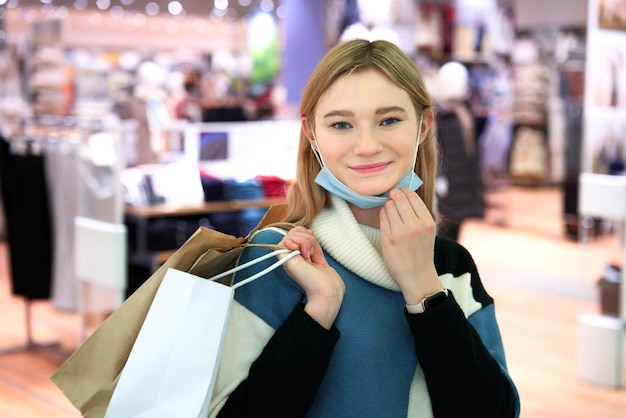 Beautiful happy girl young woman is carrying holding shopping bags in hands in mall take off mask