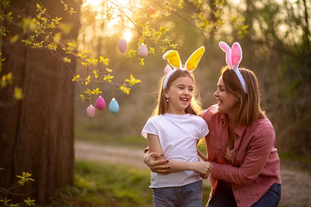 Beautiful and happy mom and daughter in bunny ears decorate the tree with easter eggs happy family celebrating easter