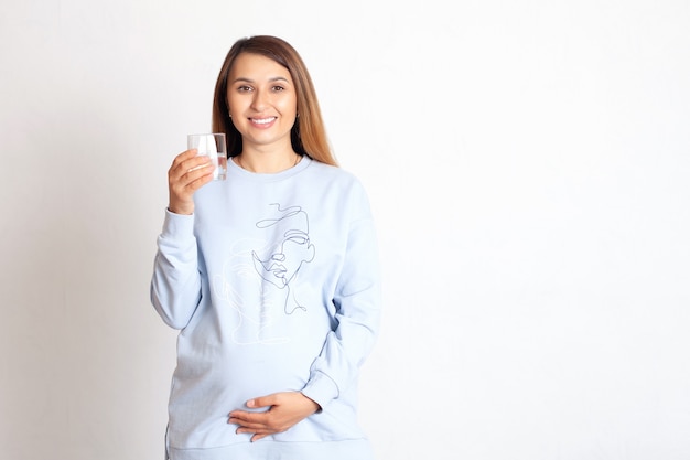 A beautiful happy pregnant woman holds a glass of water in her hand and smile