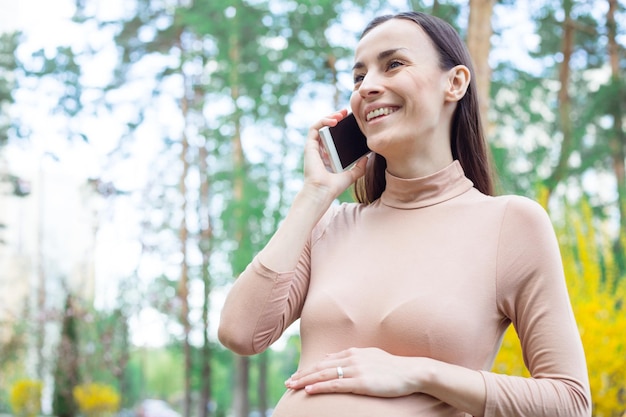 Beautiful Happy Pregnant Woman Standing Outdoors in City Park and Talking on the Phone Motherhood Pregnancy