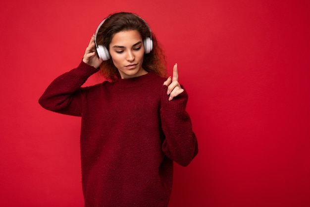 beautiful happy smiling young brunette curly woman wearing dark red sweater isolated over red